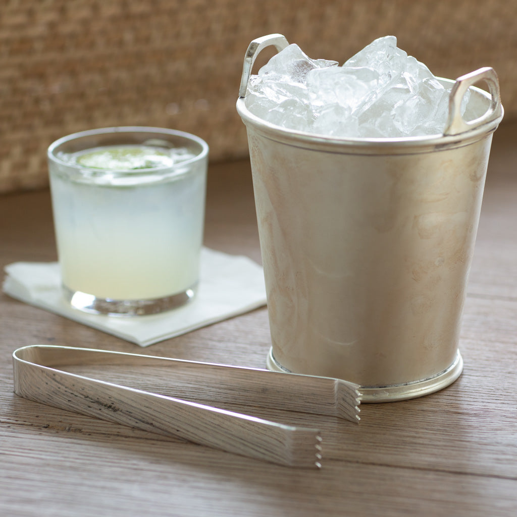 Silver ice bucket with silver tongs and cocktail